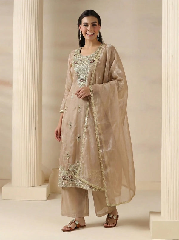 Woman wearing a beige embroidered traditional outfit with a dupatta in a classical setting.